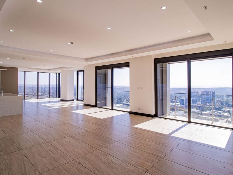 Spacious open-plan living area featuring large sliding glass doors, modern tiled flooring, recessed lighting, and a central kitchen island with panoramic city views.