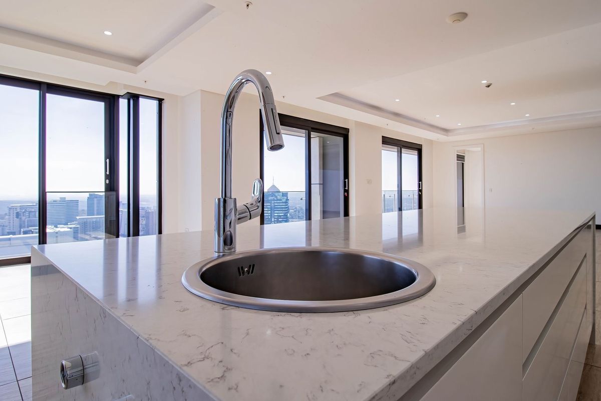 Modern kitchen island featuring a stone countertop, undermount sink, and gooseneck faucet, set within an open-plan living space with expansive city views.