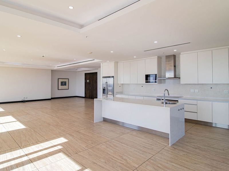Spacious open-plan living area featuring a modern kitchen with white cabinetry, stone countertops, a central island, and integrated appliances.