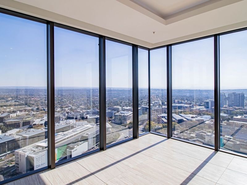 A bright, empty living area featuring expansive floor-to-ceiling windows that offer panoramic city views and modern tiled flooring.