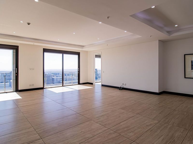 Spacious, light-filled living area featuring modern tiled flooring, recessed ceiling lights, and large sliding glass doors opening to a balcony with city views.