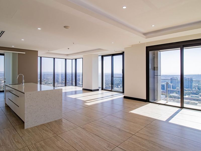 Spacious open-plan living area featuring a modern kitchen island, floor-to-ceiling windows with panoramic city views, and access to a private balcony.