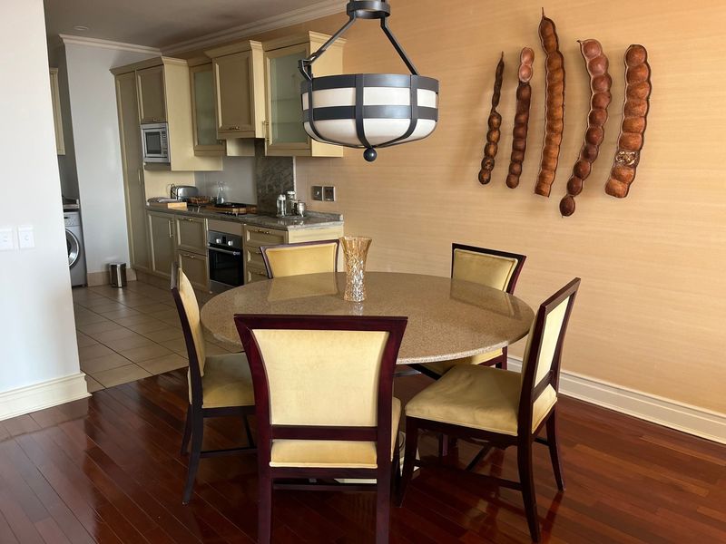 Open plan dining area featuring hardwood floors and a modern pendant light, adjacent to a functional kitchen with built-in cabinetry and granite countertops.