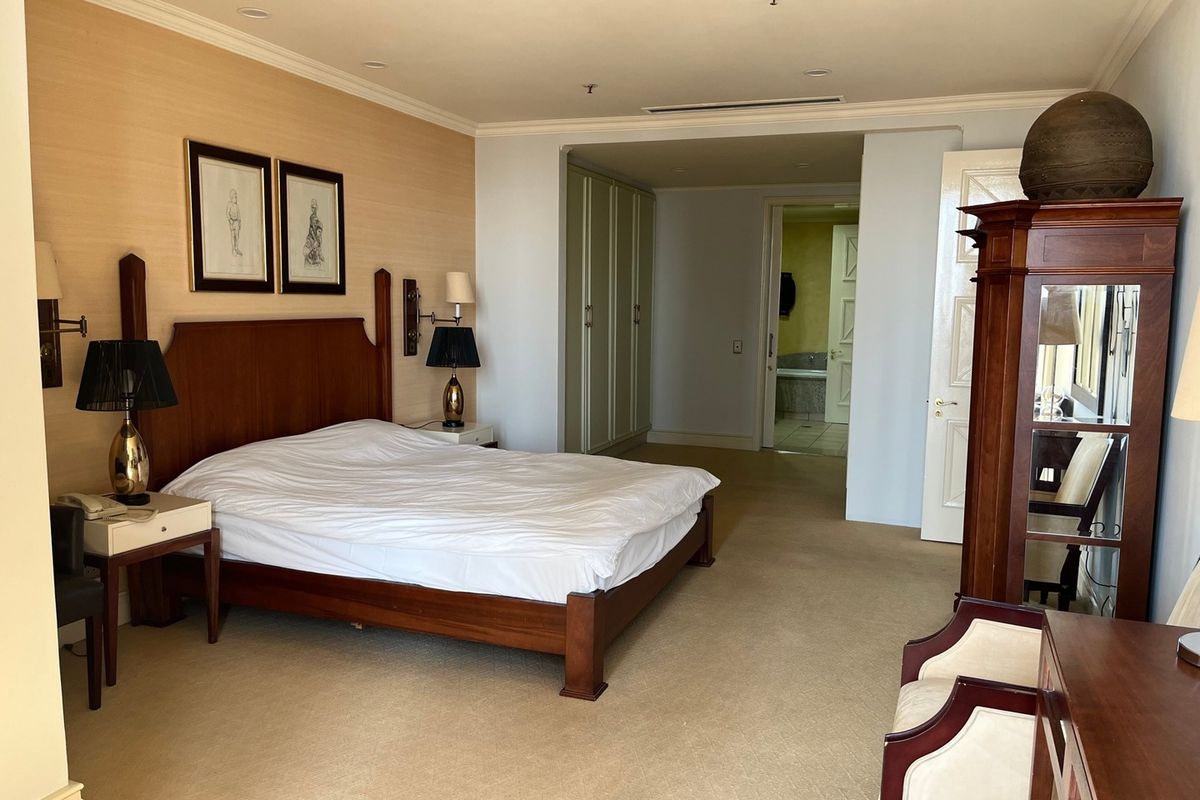 Spacious bedroom featuring built-in cupboards, textured wallpaper, and carpeted flooring, with an adjoining en-suite bathroom visible through the doorway.