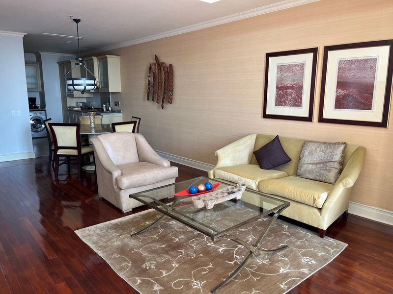 Open plan living and dining area featuring polished hardwood floors, crown molding, and an integrated kitchen with built-in cabinetry and appliances.