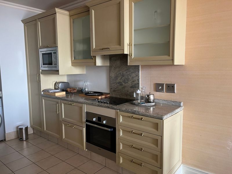 A functional kitchen featuring light-toned cabinetry, granite countertops, integrated oven, electric cooktop, and built-in microwave with tiled flooring.