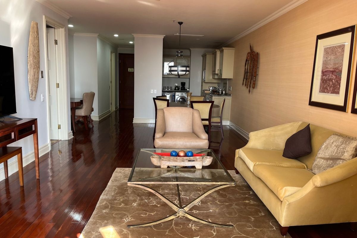 Open-plan living area featuring polished hardwood floors, crown molding, and a compact kitchen with integrated cabinetry and laundry facilities.
