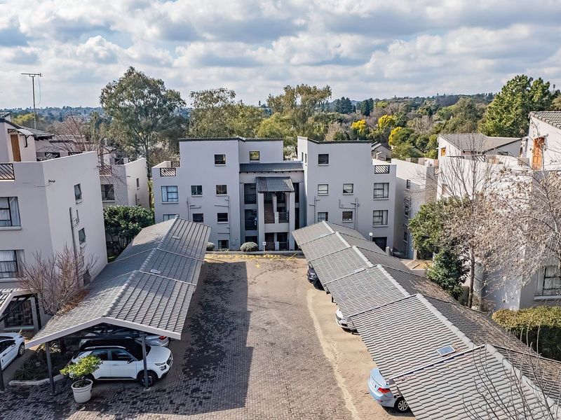 Aerial view of an apartment complex featuring multiple residential blocks, paved driveway, and covered parking bays.
