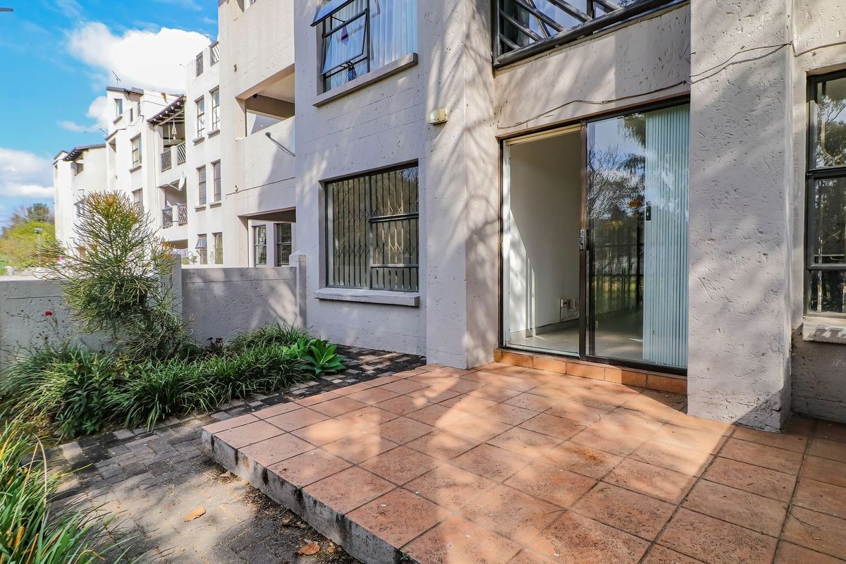 A ground floor apartment exterior featuring a tiled patio area, sliding glass door access, and a small landscaped garden space.
