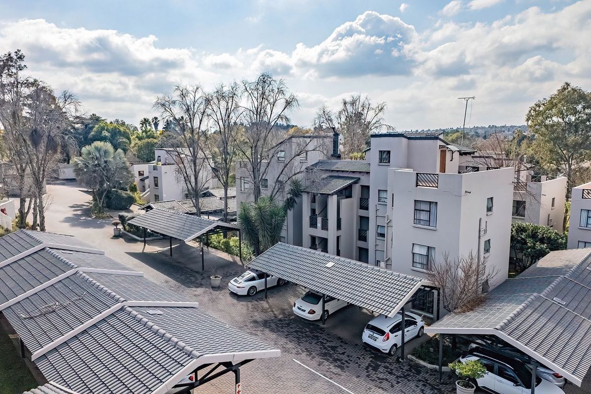 Aerial view of an apartment complex featuring multiple residential buildings, paved driveways, and covered parking carports.