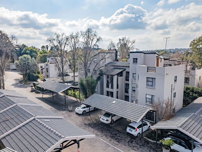 Aerial view of an apartment complex featuring multiple residential buildings, paved driveways, and covered parking carports.