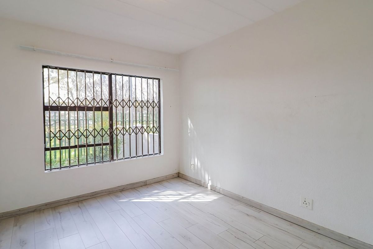A bright, empty bedroom featuring light-toned laminate flooring and a window fitted with a security gate.
