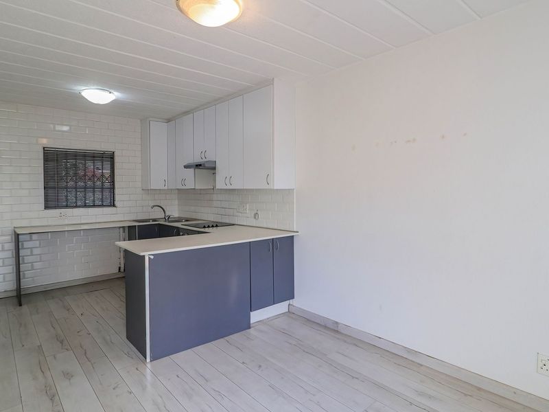 A functional, empty kitchen featuring white subway tile backsplashes, laminate flooring, and a practical peninsula layout with built-in cabinetry and essential appliances.