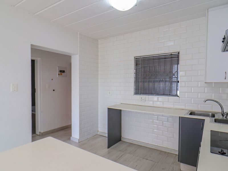 A functional kitchen featuring a white subway tile backsplash, stainless steel sink, extractor fan, and laminate flooring with built-in cabinetry.