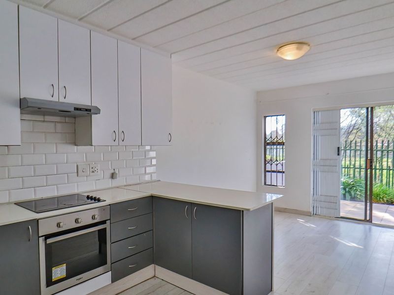 Open-plan kitchen and living area featuring modern two-tone cabinetry, subway tile backsplash, built-in appliances, and direct access to a private patio through sliding doors.
