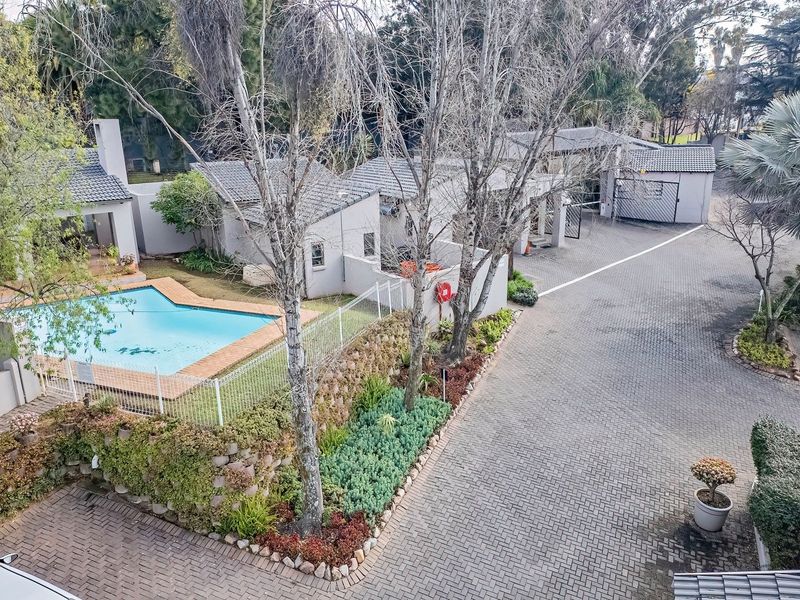 Aerial view of the apartment complex grounds, featuring a swimming pool, paved driveway, and established garden areas.