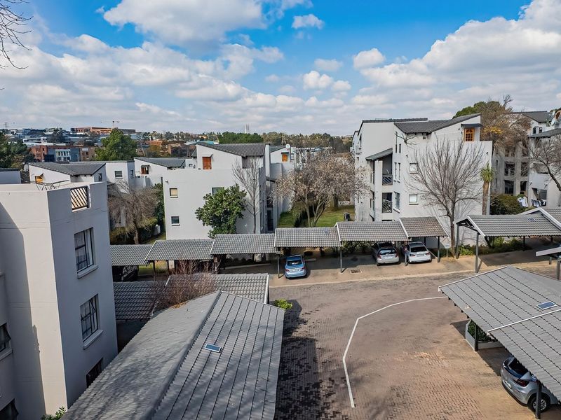 An elevated aerial view of an apartment complex featuring multiple residential buildings, paved driveways, and covered carport parking structures.