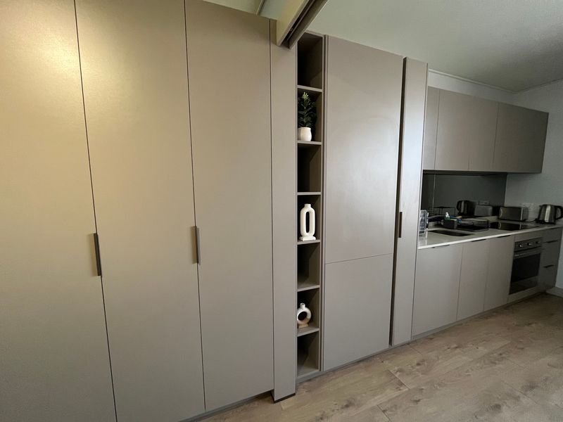 Modern kitchen featuring sleek taupe built-in cabinetry, integrated oven, stone countertops, and open shelving, complemented by durable laminate flooring.