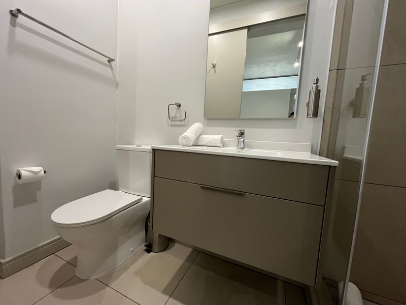 Modern bathroom featuring a wall-mounted vanity with integrated basin, sleek mixer tap, toilet, and a glass-enclosed shower area with neutral floor tiling.