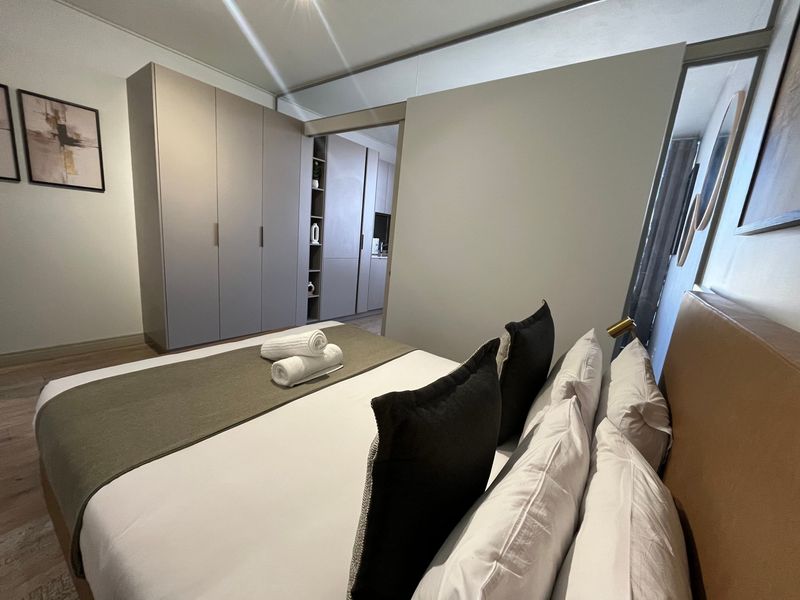 A modern bedroom featuring sleek built-in cupboards, laminate flooring, and a sliding door leading to an adjacent space.