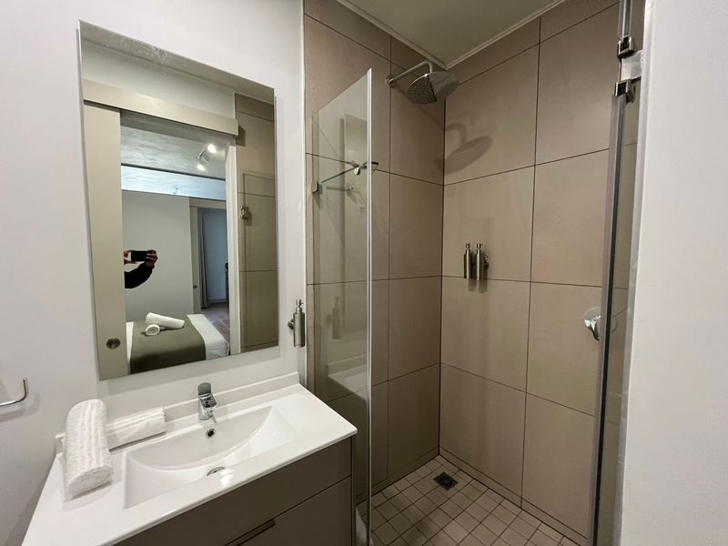 Modern bathroom featuring a vanity with integrated basin, wall-mounted mirror, and a walk-in shower with glass screen and neutral tiling.