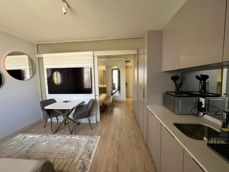 Modern open-plan apartment featuring a compact kitchen with built-in cabinetry, laminate flooring, and a seamless transition to the living and bedroom areas.