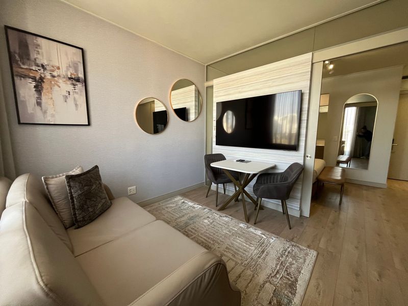 A modern, well-maintained living area featuring laminate flooring, a wall-mounted television, and a sliding door leading to an adjacent bedroom space.