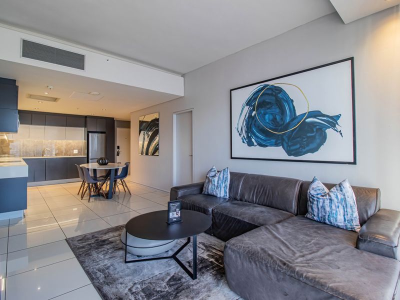 Modern open-plan apartment featuring a sleek kitchen with stone countertops and integrated cabinetry, flowing seamlessly into a comfortable living and dining area.