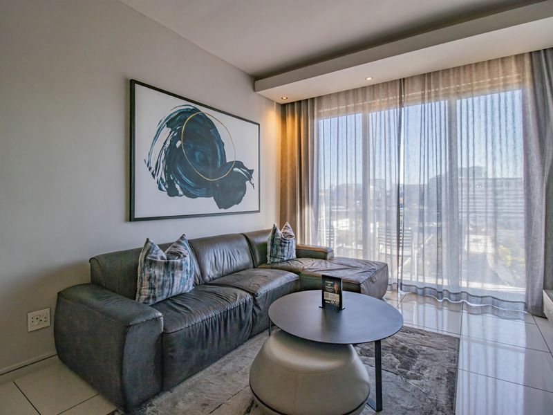 A modern living room featuring tiled flooring, recessed ceiling lighting, and a large glass sliding door with floor-to-ceiling curtains providing natural light.