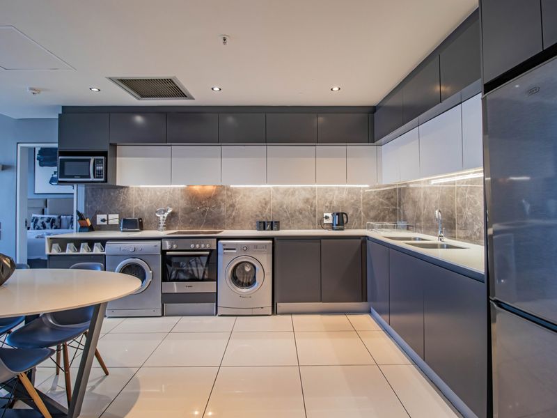 Modern kitchen featuring sleek two-tone cabinetry, stone-look backsplash, integrated appliances, and high-quality tiled flooring in an open-plan layout.