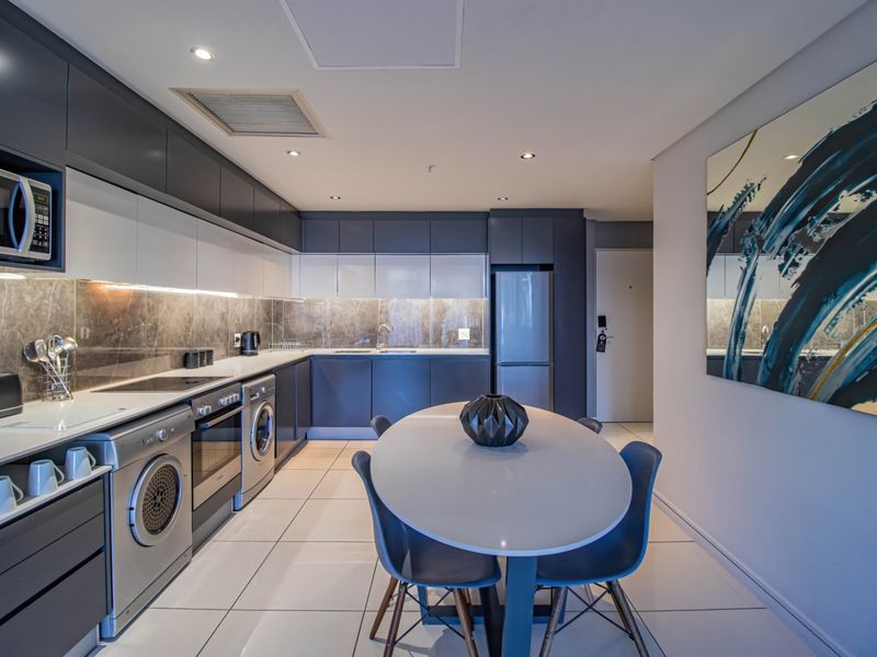 Modern open-plan kitchen featuring sleek two-tone cabinetry, stone backsplash, integrated appliances, and tiled flooring, seamlessly flowing into the dining area.