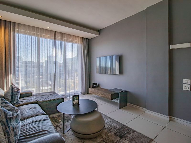 A modern living room featuring large floor-to-ceiling windows, recessed ceiling lighting, and neutral tiled flooring, creating a bright and contemporary atmosphere.