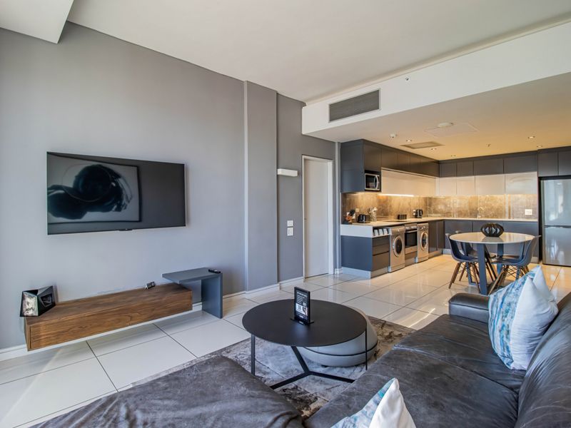 Modern open-plan living area featuring a sleek kitchen with integrated appliances, high-gloss cabinetry, and polished tiled flooring throughout.