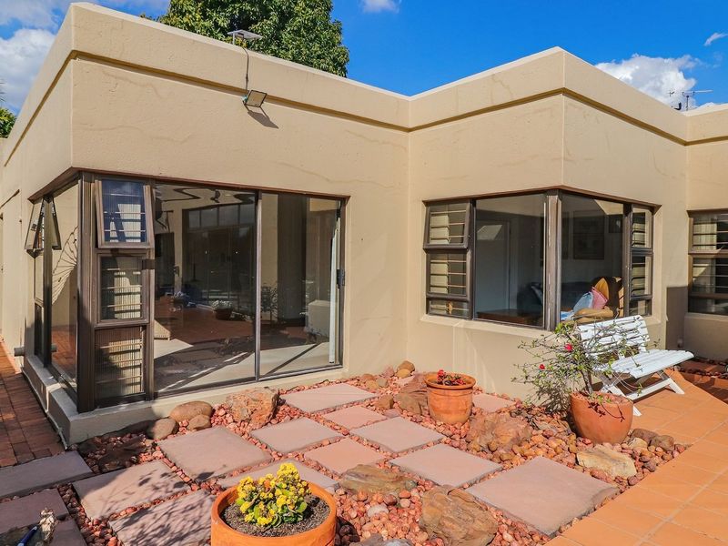 A rear exterior view of the property featuring a paved patio area, sliding glass doors, and large windows providing access to the interior living space.