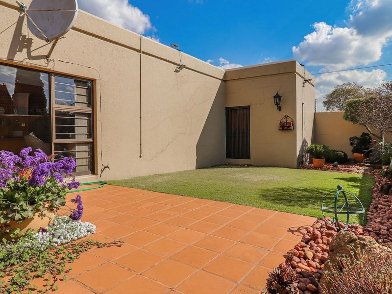 A private rear courtyard featuring a terracotta tiled patio, a small lawn area, and established garden beds against the exterior wall.