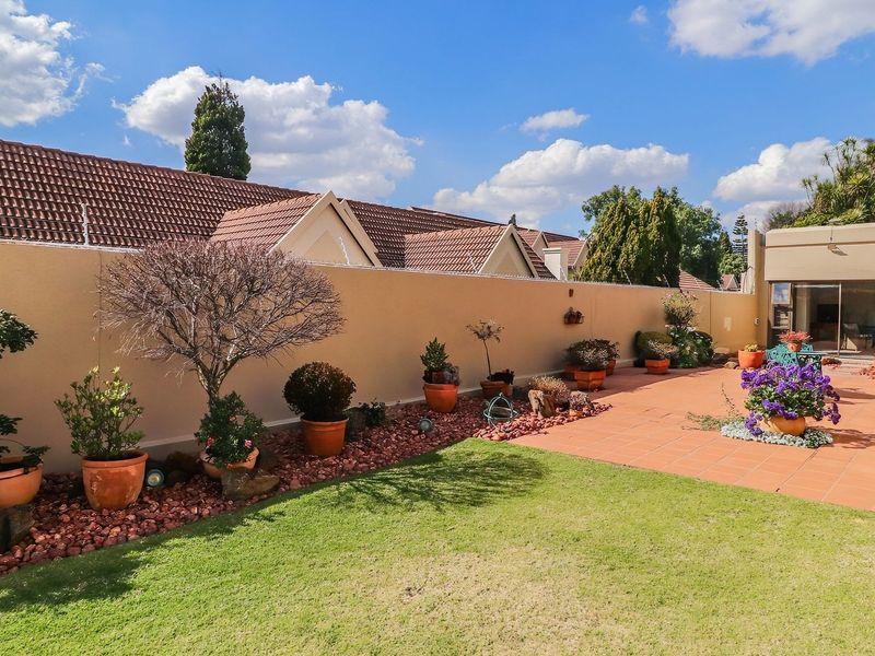 A well-maintained rear garden featuring a paved patio area, a manicured lawn, and a high perimeter wall for privacy.