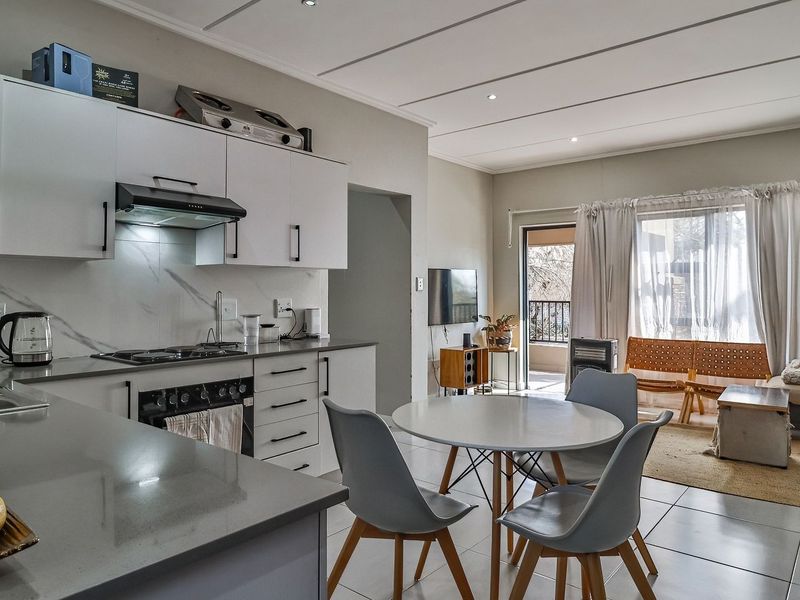 Modern open-plan kitchen and living area featuring sleek cabinetry, stone countertops, gas hob, and direct access to a private balcony.