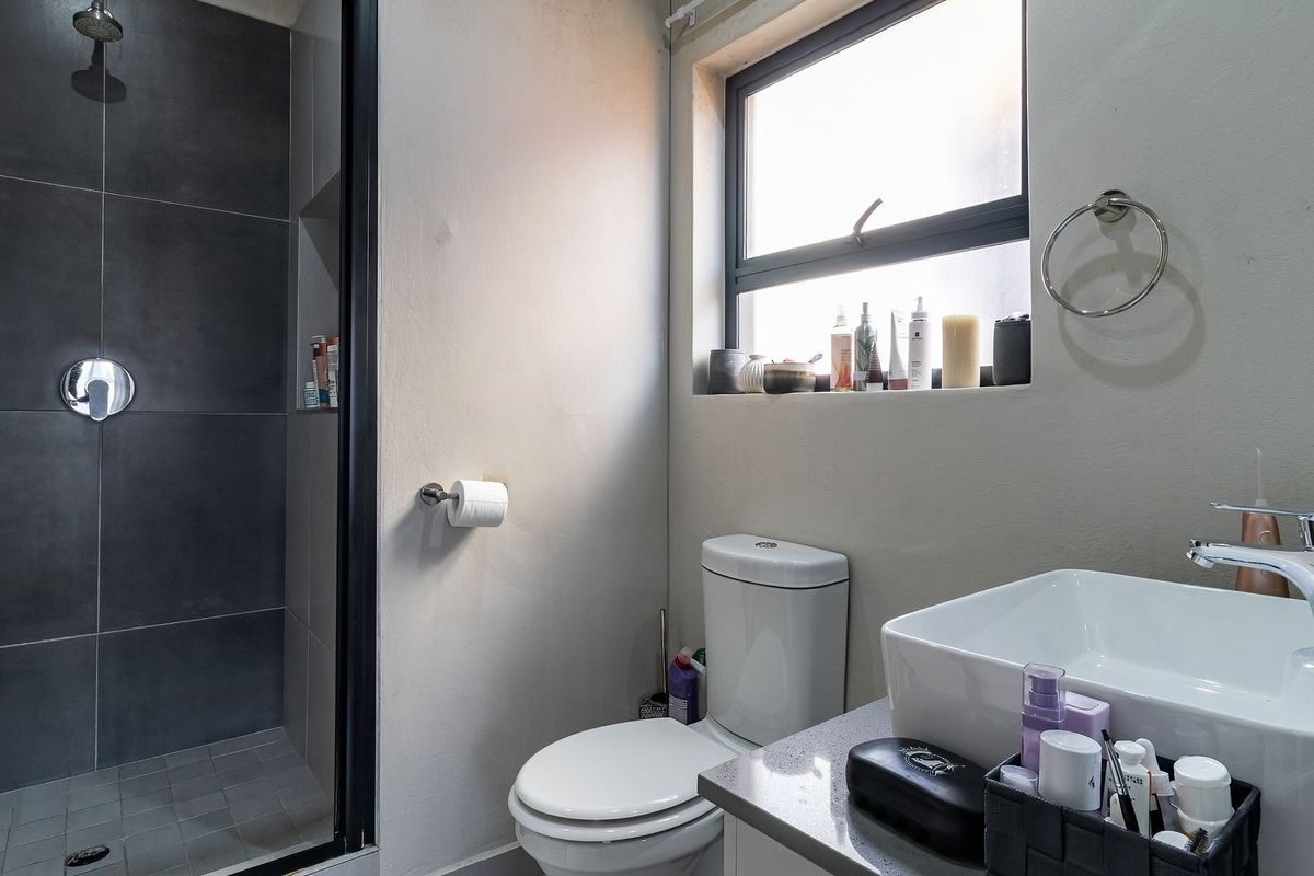 Modern bathroom featuring a walk-in shower with dark tiling, a white vessel sink on a vanity countertop, and a standard toilet.