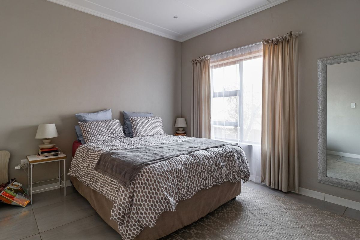 A well-maintained bedroom featuring neutral wall tones, tiled flooring, and large windows with curtain tracks, offering a clean and functional living space.