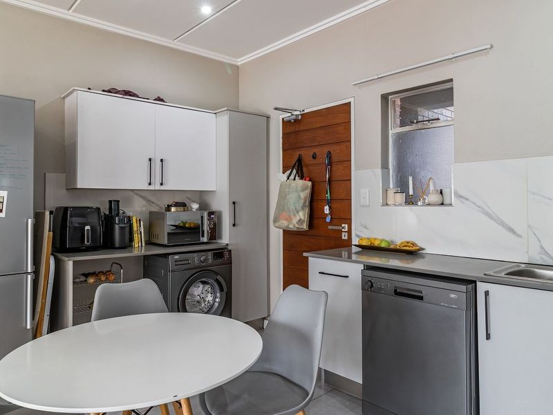 A functional kitchen featuring modern white cabinetry, marble-look splashbacks, integrated appliances, and a timber door leading to the exterior.