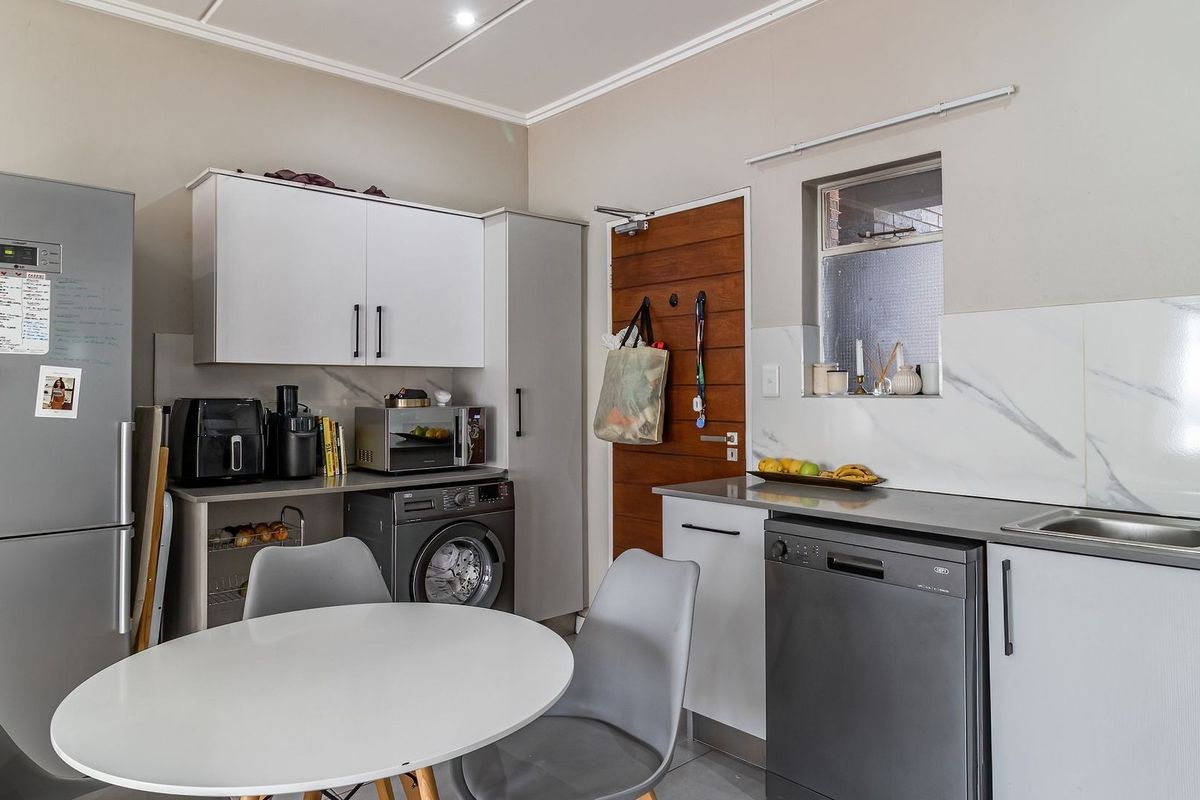 A functional kitchen featuring modern white cabinetry, marble-look splashbacks, integrated appliances, and a timber door leading to the exterior.