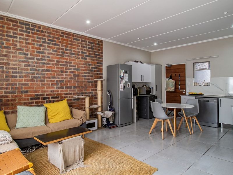Open-plan living and kitchen area featuring an exposed brick feature wall, modern tiled flooring, and functional kitchen cabinetry with integrated appliances.