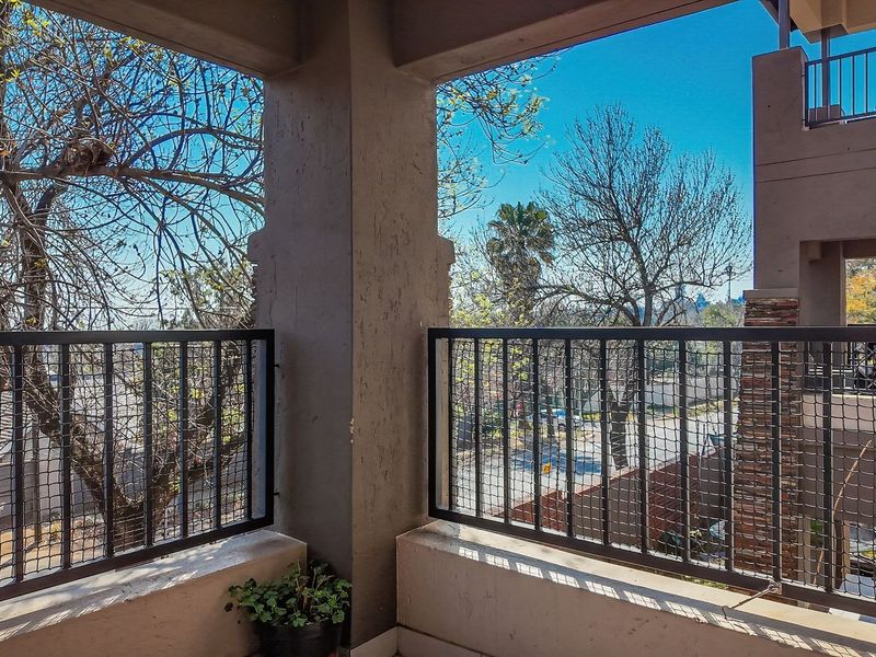 A covered balcony featuring metal balustrades with safety netting, concrete pillars, and views of the surrounding neighborhood.