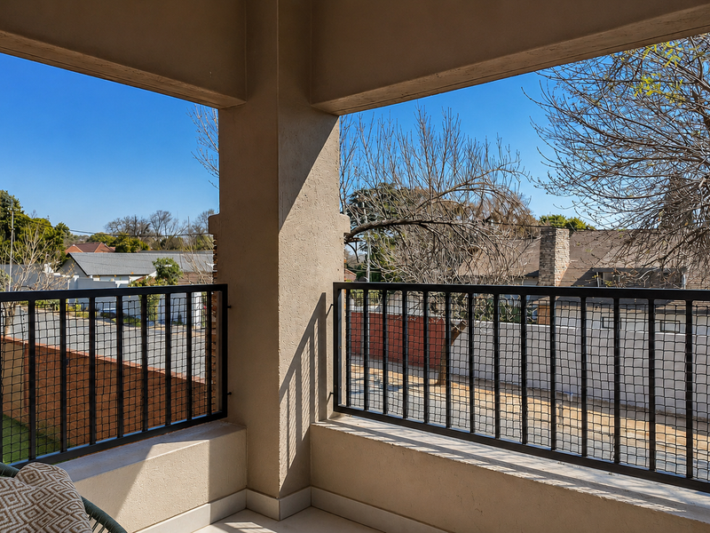 A covered balcony featuring a secure metal balustrade and tiled flooring, offering an open view of the surrounding neighborhood.
