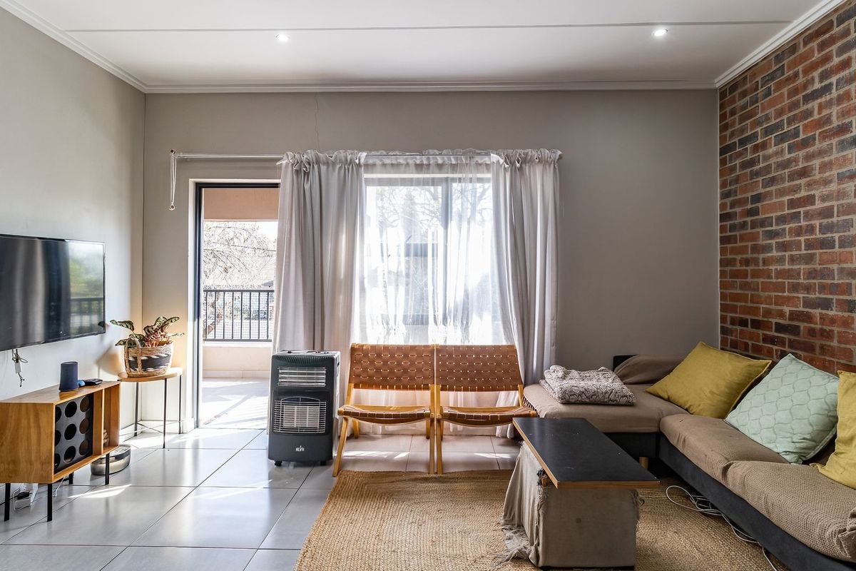 Living room featuring an exposed brick accent wall, tiled flooring, and direct access to a balcony through a sliding glass door.