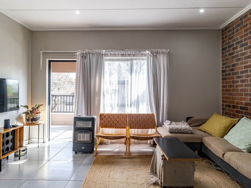 Living room featuring an exposed brick accent wall, tiled flooring, and direct access to a balcony through a sliding glass door.