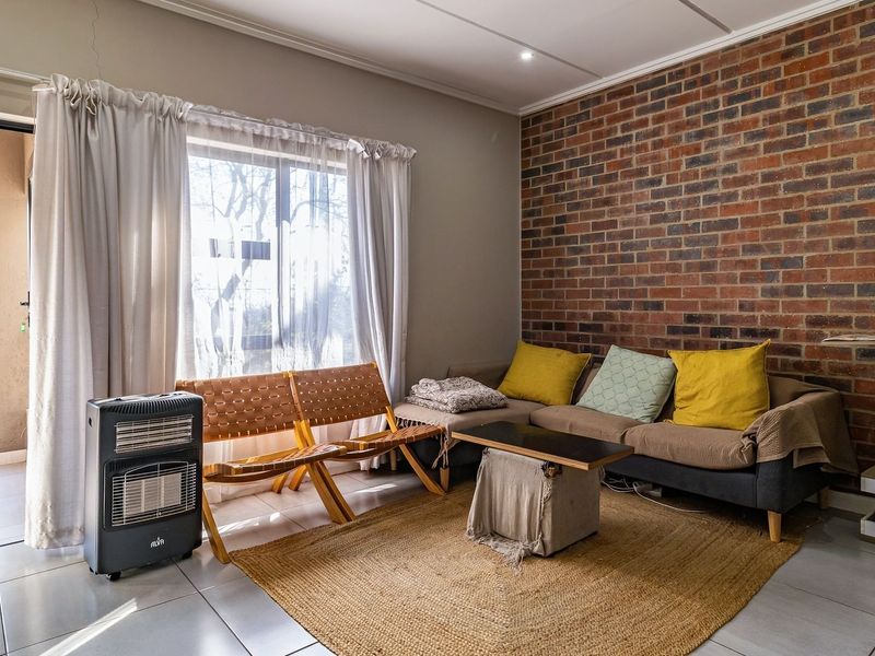 Living room featuring an exposed brick accent wall, tiled flooring, and direct access to an outdoor balcony through a sliding glass door.