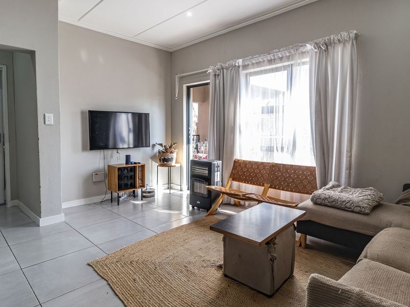 A bright living room featuring neutral tiled flooring, recessed ceiling lighting, and a sliding glass door providing access to the outdoor area.