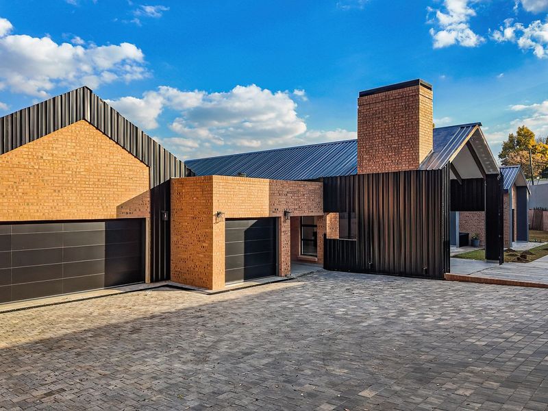 Modern architectural home featuring a striking brick and metal facade, double garage, paved driveway, and a private swimming pool.