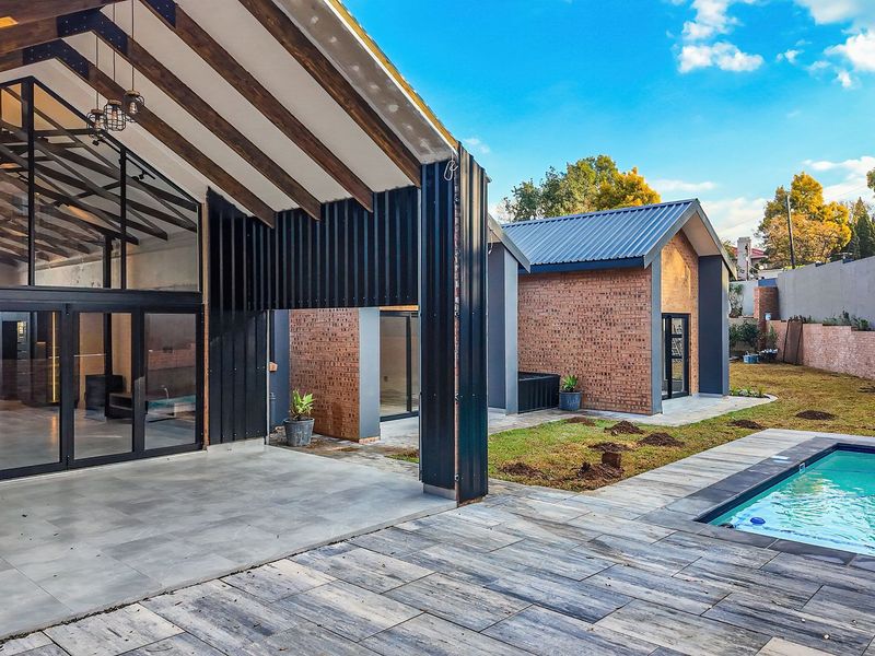 Modern rear exterior featuring a covered patio, swimming pool, and contemporary architectural design with exposed timber beams and brick finishes.
